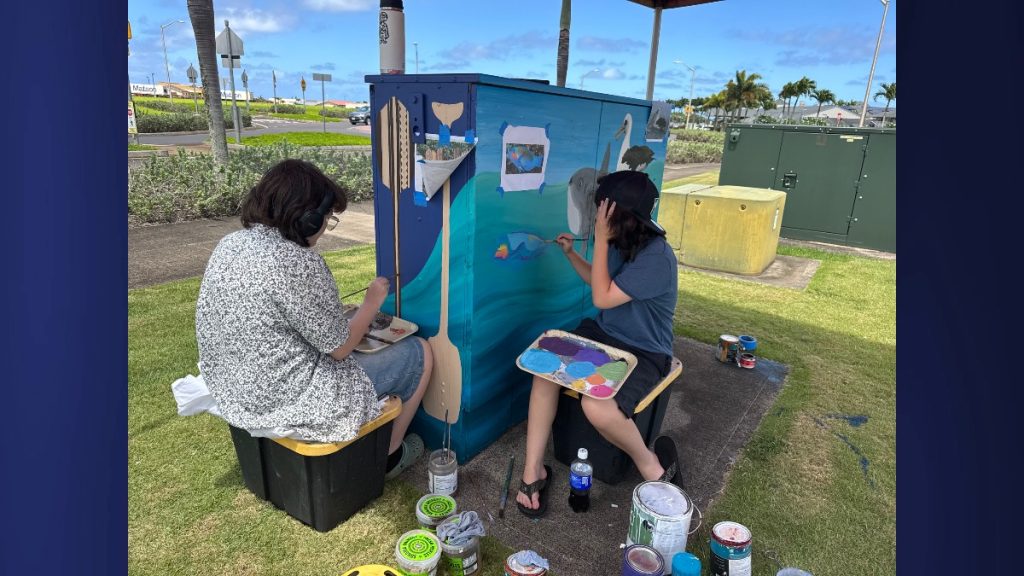 Zillary Watts (left) and Tawehi Oana-Makanani are focused on painting the sharks, sea turtles, and humpback whales at the Po'ipū box. (Photo Credit: Kayti Lathrop)