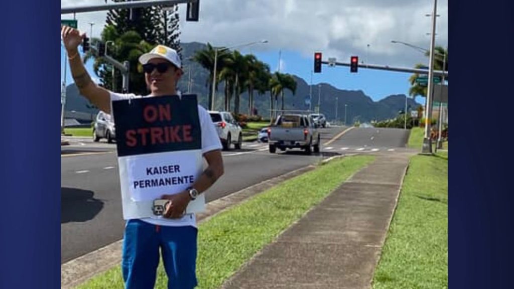 On the first day of the nationwide Kaiser Permanente strike, cars honk in solidarity while a Kaiser employee waves a shaka. (Photo Credit: Xiomara Yamileth/ Kauaʻi Now)