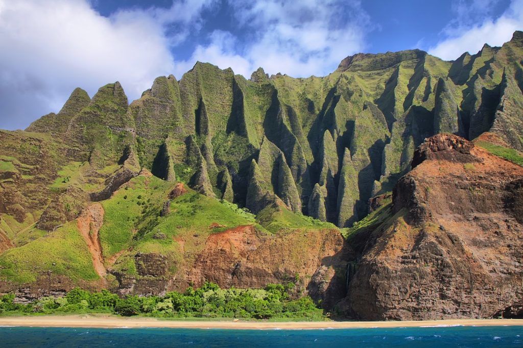 Towering emerald cliffs of the Nāpali Coast rise dramatically above the Pacific, a breathtaking view that makes every season a perfect time to visit Kaua‘i.