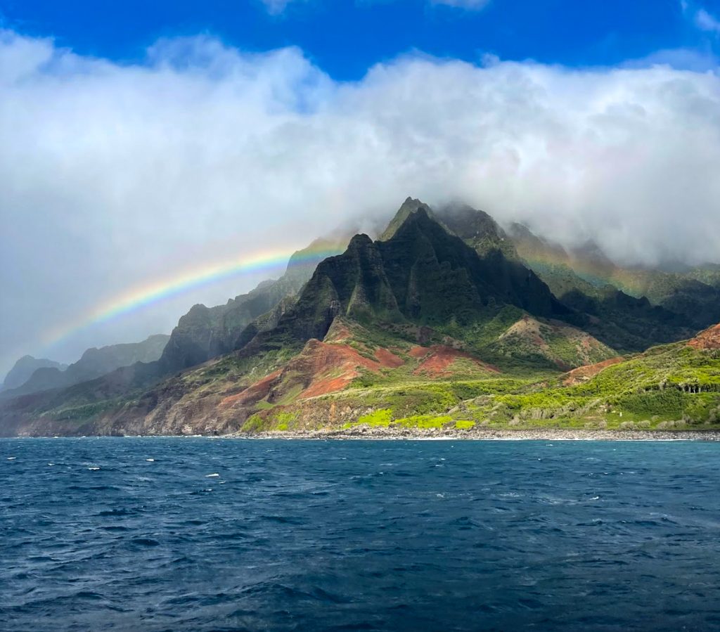 Mist clings to the jagged spires of the Nāpali Coast as a rainbow traces the ridgeline, a fleeting gift brought by a rain storm. (Photo Credit: Ilana Maxwell)